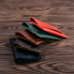 Five handmade leather cardgolders on wooden background lie one on another. Stock photo with blurred background.
