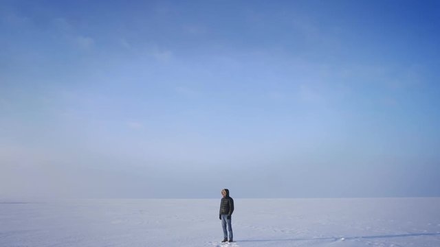 Zooming in shot of middle-aged explorer turns to camera and smiles into it on snow desert background.