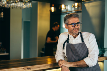 senior barman standing beside counter and looking away in cafe bar