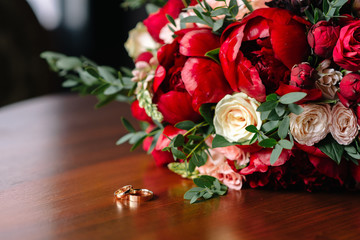 the bride's bouquet of red roses and wedding rings are on the table