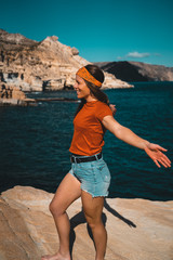 profile of a young hippie woman with open arms looking at the sea from a cliff