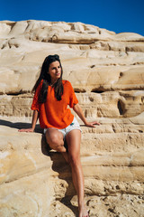 Attractive young brunette woman sitting on a cliff on the shore of the beach