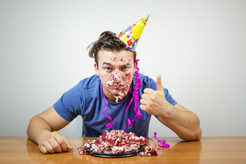 Portrait unhappy good-looking birthday guy with cake on face showing thumb up, unhappy with...