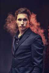 Portrait of an expressive, stylish, young man in a strict suit in orange tones with a smoky...