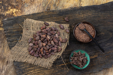 Cacao beans, cacao powder and chocolate on a piece of burlap on old plank over a wooden background