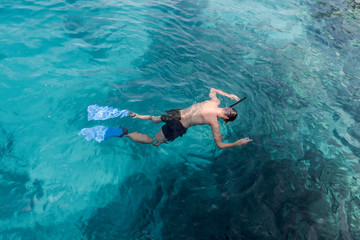 young man swimming and snorkeling with mask and fins in clear blue water