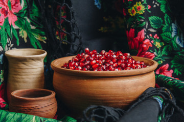 pomegranate grains in a ceramic bowl on a vintage fabric background, pomegranate fruit, ceramic jug, ceramic plate, ethnic shawl, Romma shawl, still life