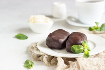 Glazed cheese curds with chocolate and mint on a white plate and a cup of coffee. Sweet breakfast or dessert. High key.