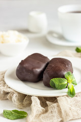 Glazed cheese curds with chocolate and mint on a white plate and a cup of coffee. Sweet breakfast or dessert. High key.