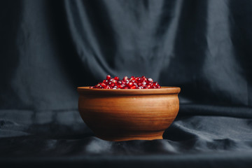 pomegranate grains in a ceramic bowl on a black fabric background, pomegranate fruit, ceramic jug, ceramic plate, isolated still life close up