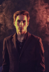Portrait of an expressive, stylish, young man in a strict suit in orange tones with a smoky background