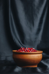 pomegranate grains in a ceramic bowl on a black fabric background, pomegranate fruit, ceramic jug, ceramic plate, isolated still life close up