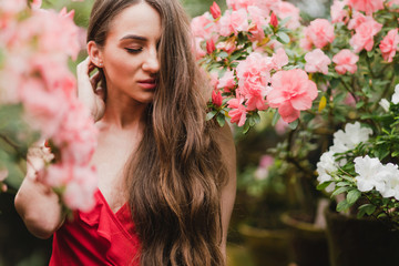 Young beautiful caucasian woman in glass greenhouse among colorful azalea flowers. Art portrait of...