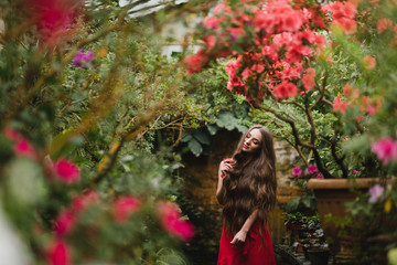 Young beautiful caucasian woman in glass greenhouse among colorful azalea flowers. Art portrait of...