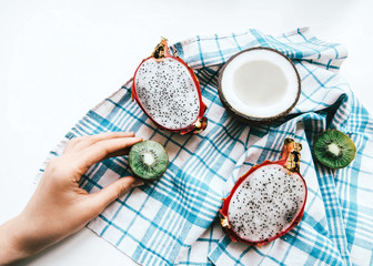 Exotic fruit Top view photo Dragon fruit, half of coconut and kiwi are lying on a white-blue checkered cotton napkin on a white table