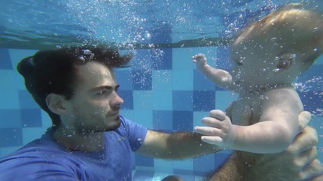 Happy smiling newborn boy is diving under water with father