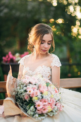 Attractive young girl in wedding dress in park posing for photographer. Bouquet of flowers