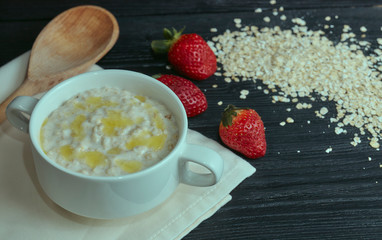Healthy and tasty breakfast. Oatmeal with strawberries on a black wooden table. horizontal view. rustic