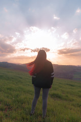 Wind is moving red hair of the girl over the hill meanwhile she is watching an awesome sunset 