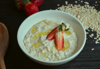 Healthy and tasty breakfast. Oatmeal with strawberries on a black wooden table. horizontal view. rustic