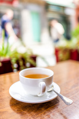 Closeup of one white teacup of green black tea in breakfast outdoor cafe restaurant outside wooden table with orange colorful vibrant vivid color cup vertical view