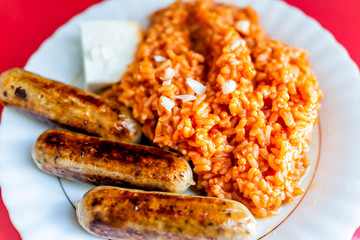 Closeup of large sausages on lunch dinner plate with fried tomato red rice, cheese cube and orange color greasy food