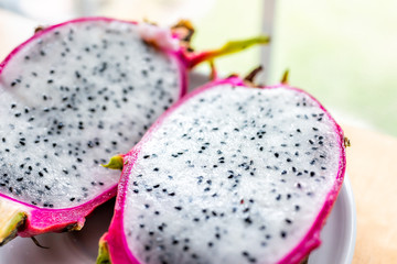 Closeup macro of cut open pink purple dragon dragonfruit fruit slices halves half inside white flesh seeds cactus on by window