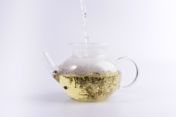 Pouring hot water to the glass teapot with herbal tea, isolated on white background