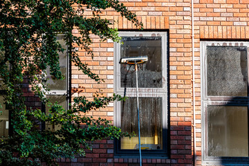 Worker cleaning washing windows on brick apartment flat with soap and water in London, UK neighborhood city