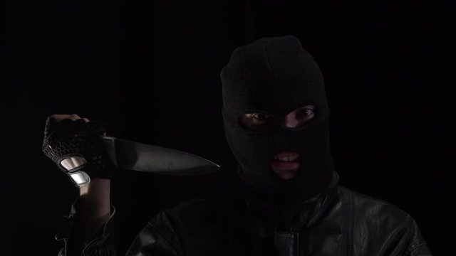 Scary criminal wearing a mask over his head showing a long knife intimidating the viewer.