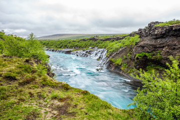 Fototapeta na wymiar Long exposure smooth colorful vibrant blue aqua turquoise water waterfall cascades Hraunfossar Lava Falls in Iceland, landscape view
