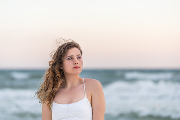 Fototapeta na wymiar Young woman in white dress on beach sunset in Florida panhandle with hair blowing in wind and bokeh of ocean waves background looking up