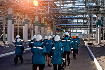 Workers of chemical factory in working clothes walks near large pipeline construction to their...