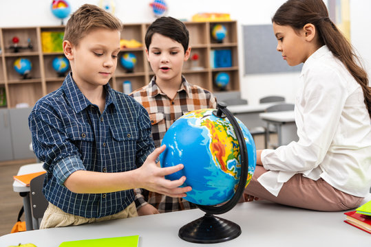 Three cheerful pupils playing with globe in classroom during geography lesson