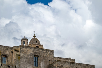 Fototapeta premium Summer blue sky and church roof with religious cross, view of ancient town of Matera, the Sassi di Matera, Basilicata, Southern Italy, cloudy summer August day