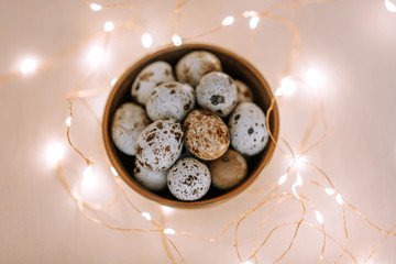 Quail eggs in a wooden plate on a pink background with golden lights. Easter concept.