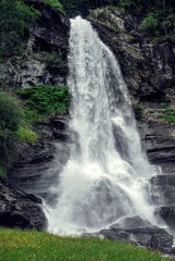 Waterfall in Norway with jagged rocks and green grass