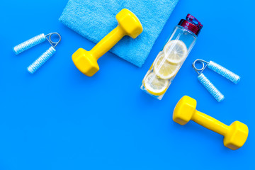 workout with bars, bottle of water, towel and wrist builder blue background top view copyspace