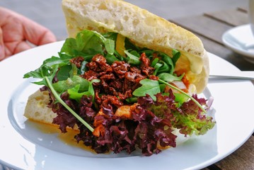 Artisan Sandwich with lettuce, sauce, on white plate with wood table 