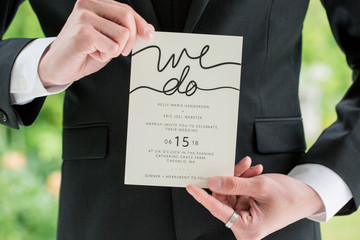 groom in black suit holding wedding invitation