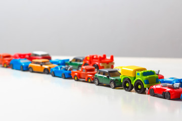 Plastic multi-colored toy cars are lined up on a white background. Stereotypical alignment of subjects is a sign of autism. Selective focus. Copy space for text. Traffic jams air pollution concept.