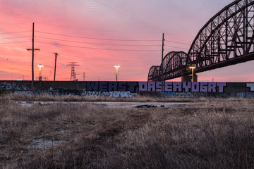 Sunrise in a brush covered industrial area with train bridge crossing over