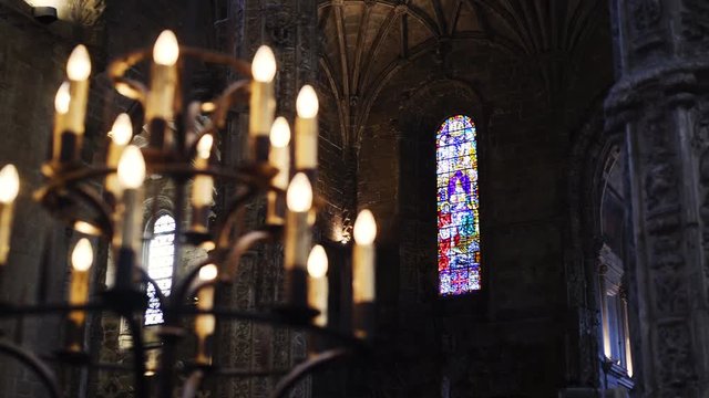 Interior medieval cathedral with ornamental columns and dark wall . Motion shot through blurred candlestick on foreground to colorful stained glass window. Portugal, Lisbon