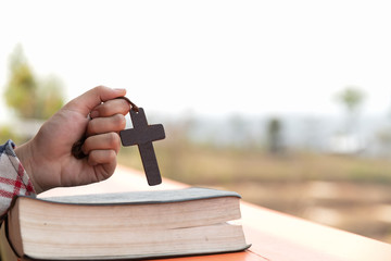 close up young hands holding wooden cross over holy bible and praying. christian concept