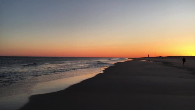 A woman walking on the beach as the sun sets over Robert Moses State Park on Fire Island, NY.