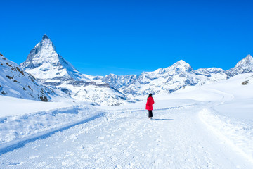 Naklejka na ściany i meble Young woman tourist walking in the snow to see beautiful Matterhorn Mountain, Zermatt, Switzerland.