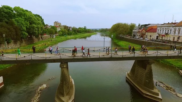 Aerial view of the central pedestrian bridge over the river floating through the city, roofscape. Picturesque landscape, citizens, enjoying the view. Drone flying footage