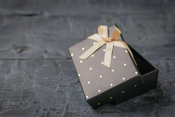 Ajar black gift box with bow on a black wooden table.