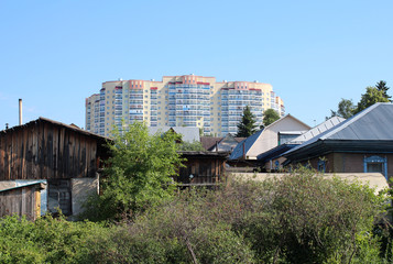 Fototapeta premium Old wooden houses with a fence on the background of new high-rise buildings under construction in the city