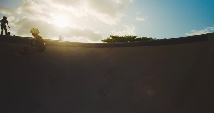 Young skateboarder kid riding a pool bowl at sunset, extreme skateboarder kid lifestyle, slow motion